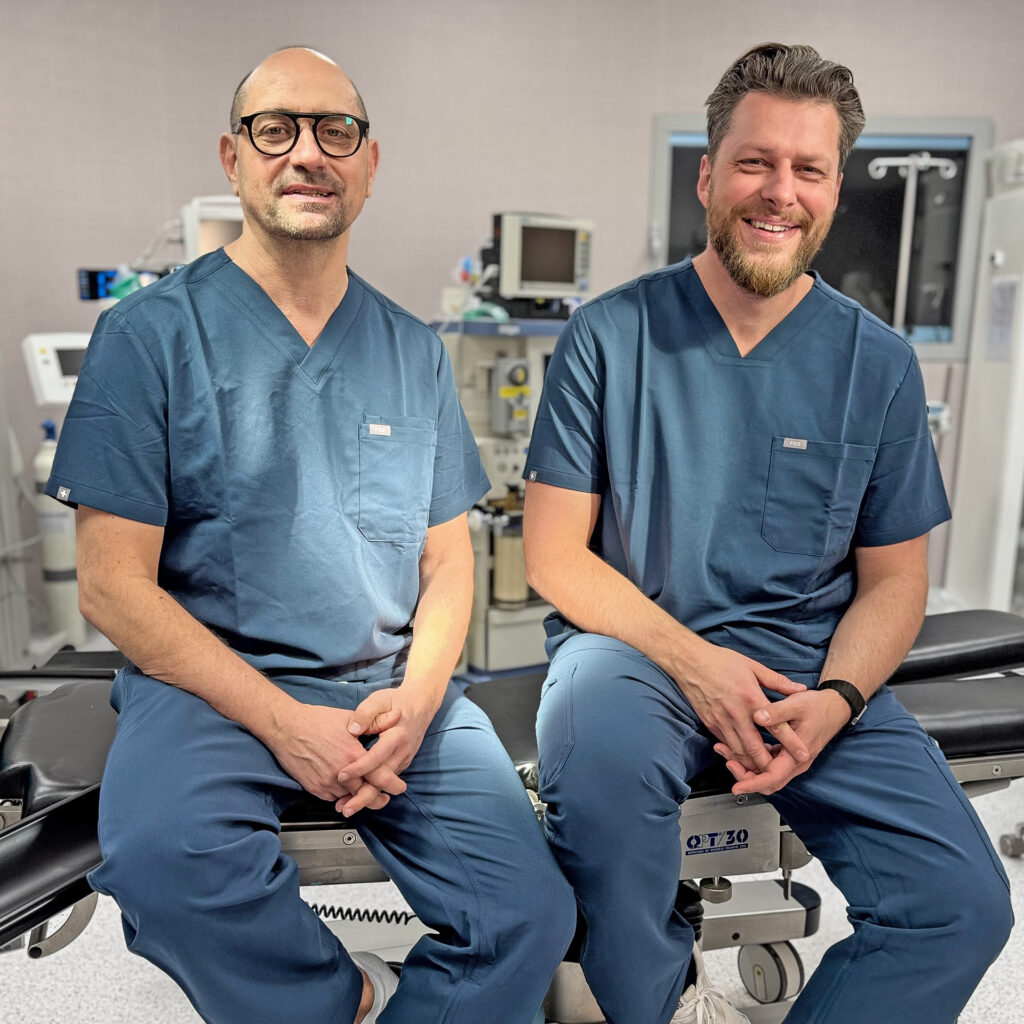 Two medical specialists in surgical scrubs sitting in a modern operating room at NOVACELL Clinic, representing the clinic’s experienced and professional medical team.